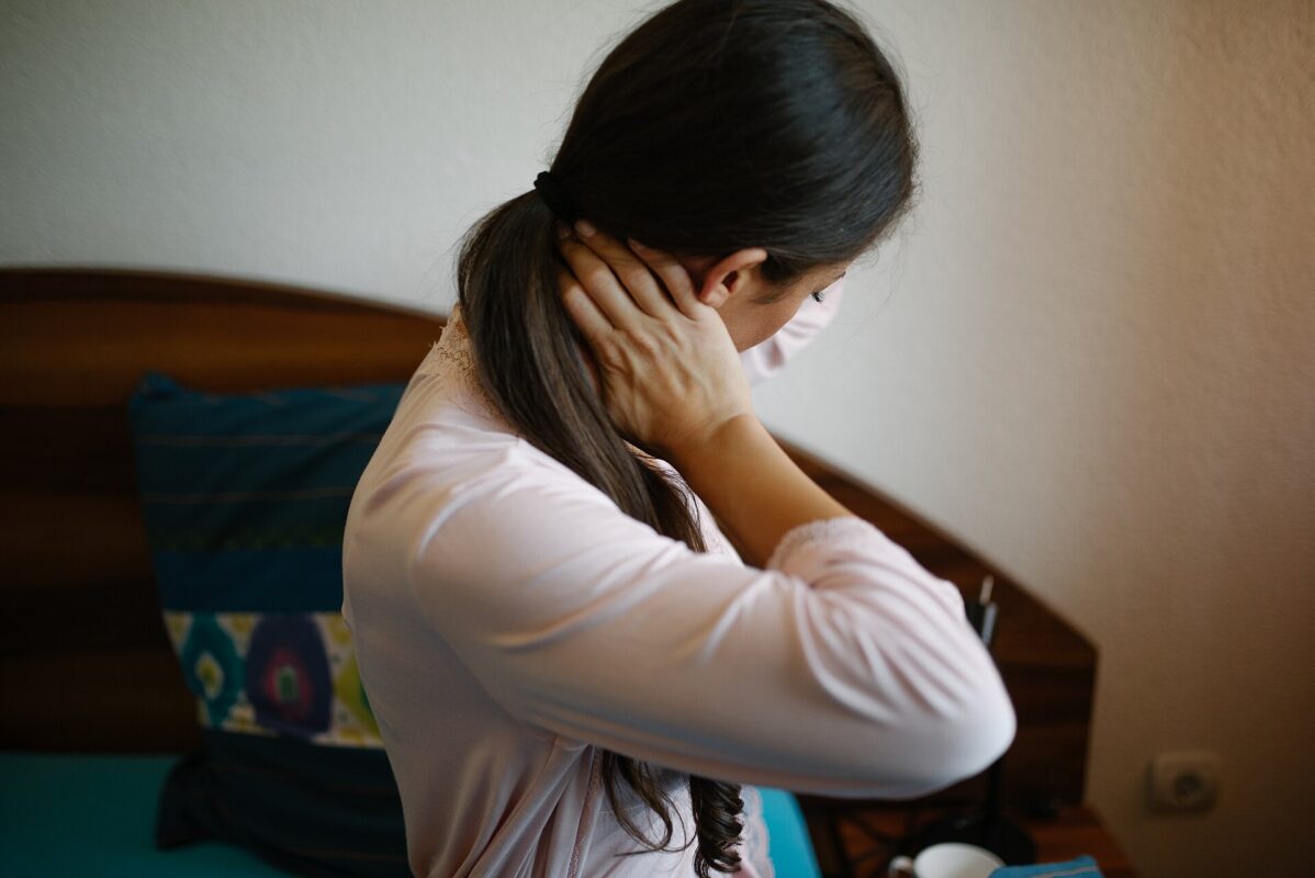 Woman sitting up in bed after waking, holding the back of her neck in pain